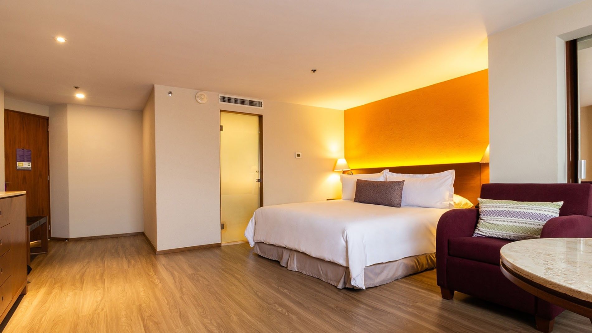 Junior Suite King con cama grande, sofá y mesa en Camino Real Aeropuerto México, Ciudad de México.