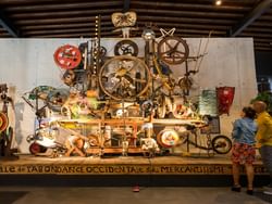 Mechanical art piece with lights and motion set against concrete at Espace Jean Tinguely near Hotel des Innovations