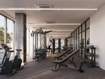 A modern gym with large windows, various exercise machines, and a person walking through.