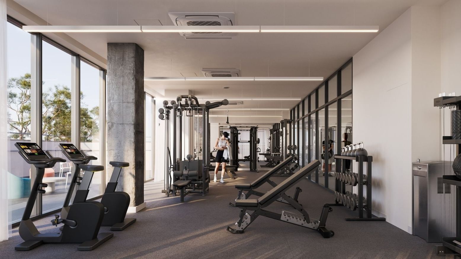 A modern gym with large windows, various exercise machines, and a person walking through.
