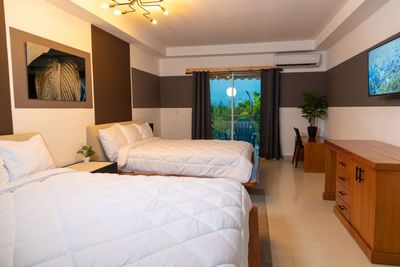Two beds facing TV and balcony seating area in Deluxe Double at MARINN Tropical Vibes Hotel
