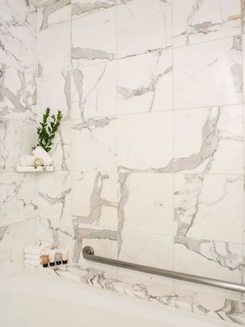 Marble tiled shower with a silver handrail by a bathtub and toiletries in Accessible Deluxe Rooms at Warwick Seattle