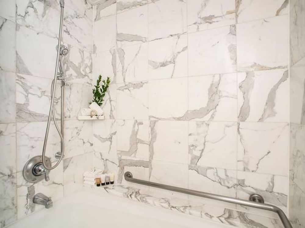 Marble tiled shower with a silver handrail by a bathtub and toiletries in Accessible Deluxe Rooms at Warwick Seattle