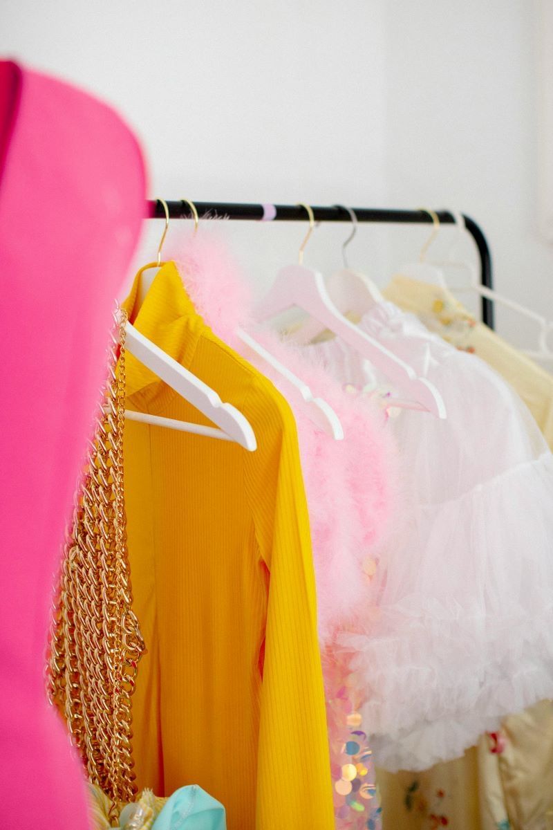 A black rack of clothing showing a few yellow, pink, and glittery pieces of clothing hanging from it. 