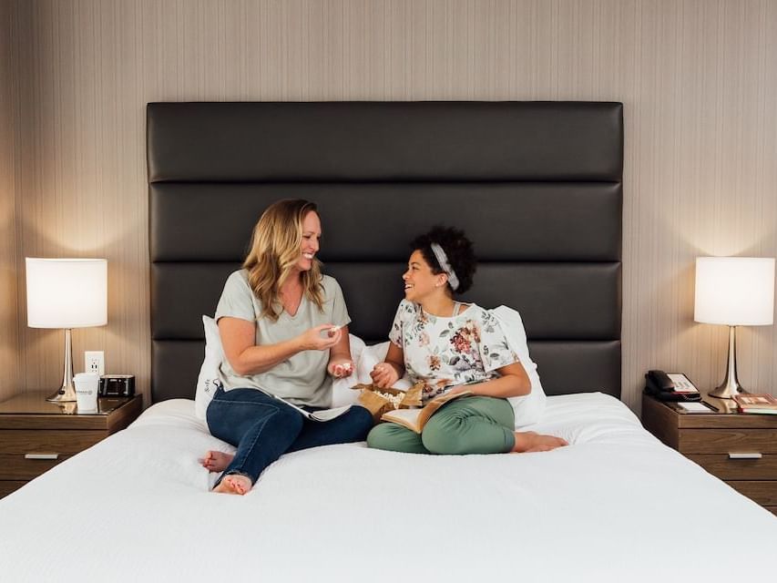 Two people sitting on bed with one person holding a book at Sandman Hotel & Suites Winnipeg Airport