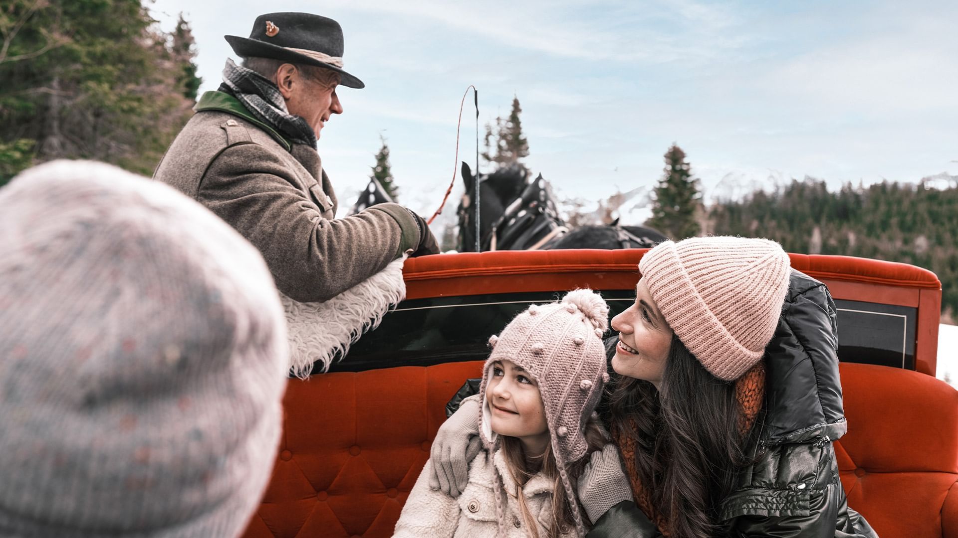 People in winter attire riding in an open red vehicle at Falkensteiner Hotels & Residences