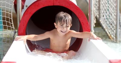 A happy young boy smiling while splashing out of a red and white closed tube water slide at Centennial Plaza Resort