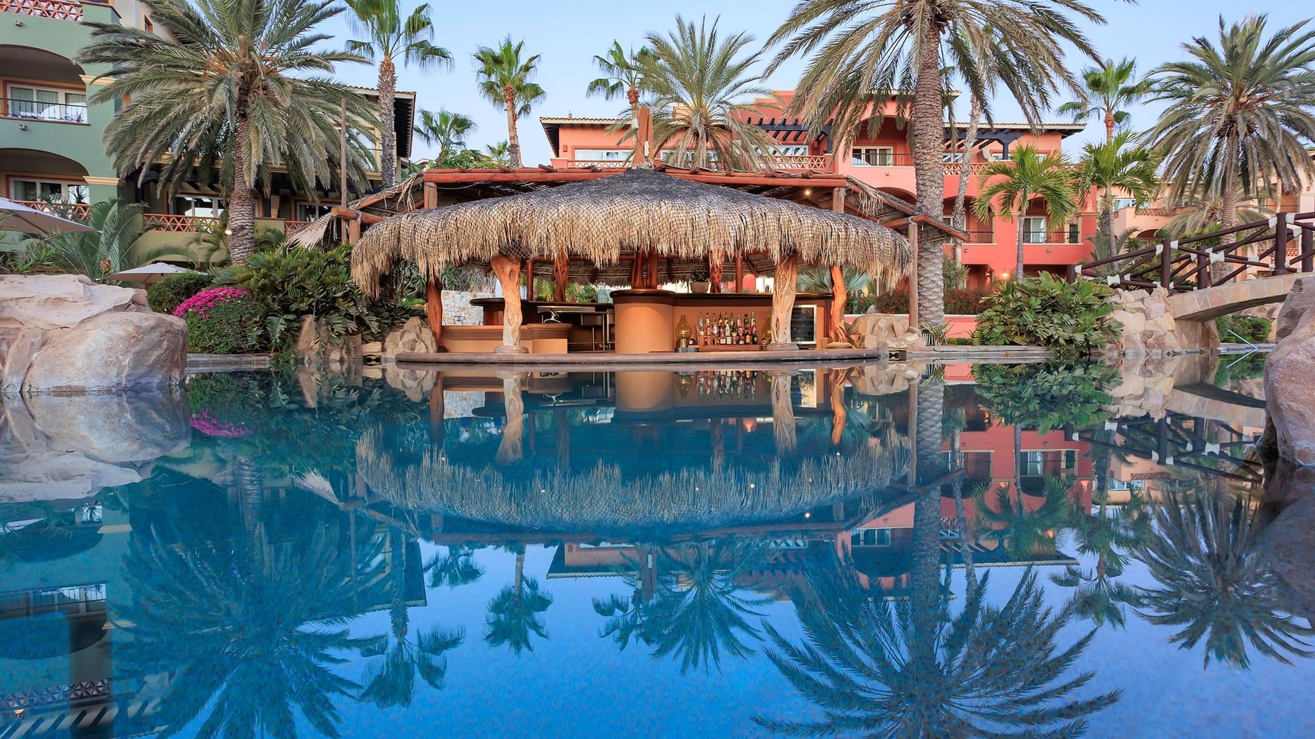 Palms reflected in a resort pool with a thatched-roof Delfines Bar at Hacienda del Mar Los Cabos.