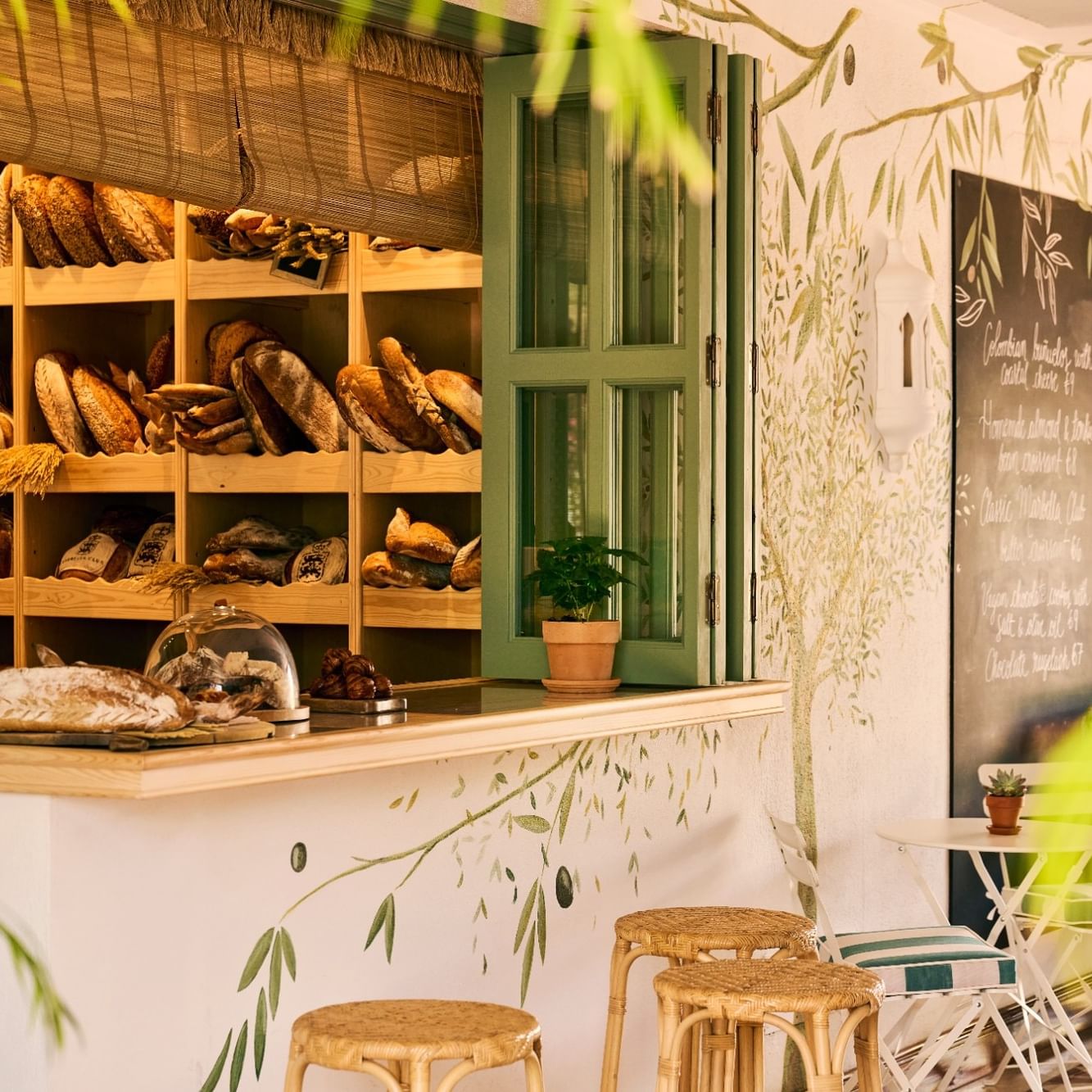 Rustic bakery display with wooden shelves showcasing artisan breads, green accents, and wicker seating at The Breakfast Club