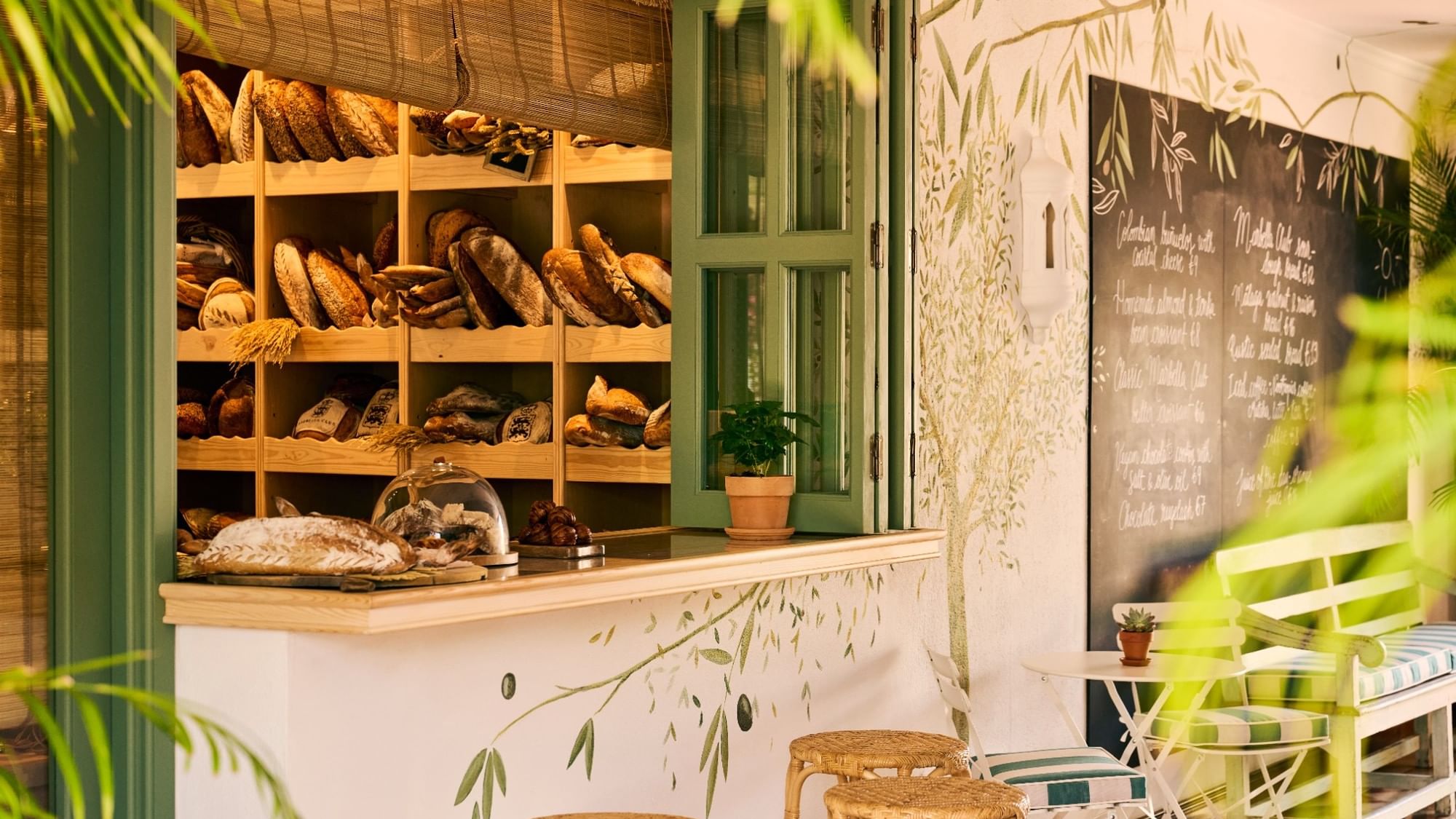 Artisan bakery display with fresh bread on wooden shelves and wicker seating at El Obrador, Marbella Club