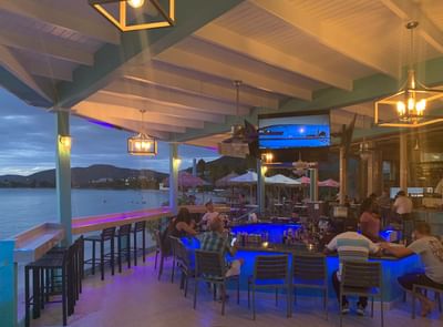 Lively evening crowd at a modern, neon-lit outdoor Emerald Beach Bar under a canopy at Emerald Beach Resort