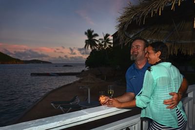 Couple enjoying a scenic sunset view from a balcony overlooking the water at the Lindbergh Bay Hotel & Villas