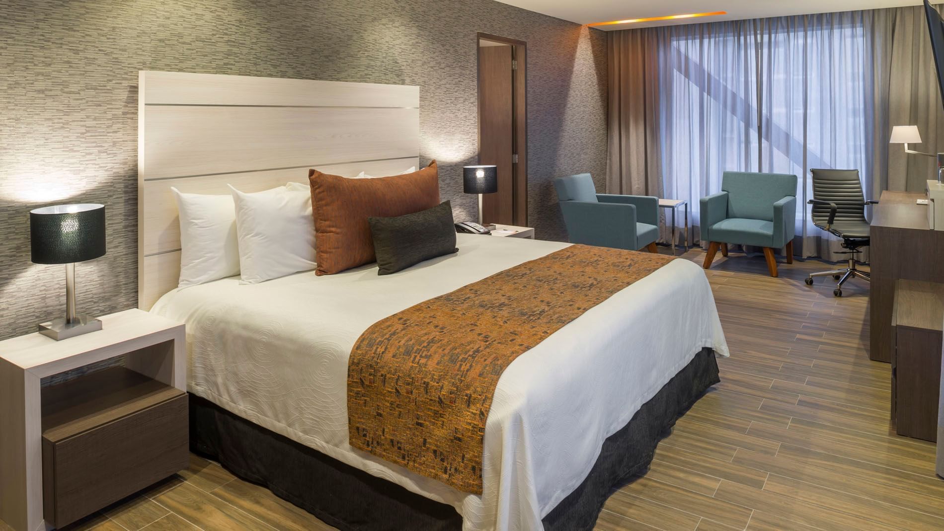 Contemporary guest room with a king bed, wood-look tile floors, and blue accent chairs at Real Inn Celaya 
