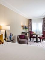 Plush bed by a round dining table and purple chairs in Family room with two queen beds at Warwick Paris Champs Elysées
