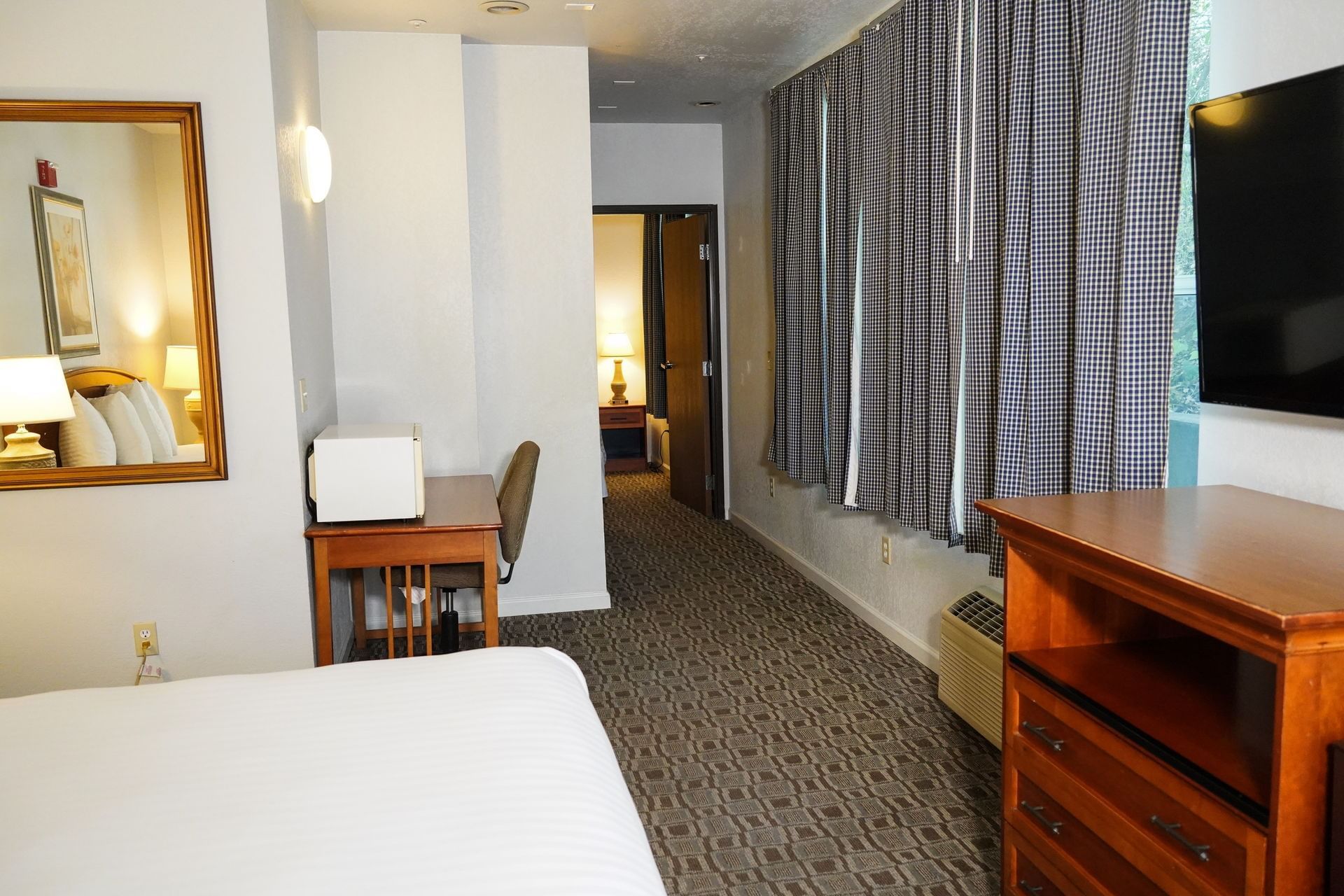 A wide-angle view of a hotel room with a bed, TV, desk, and mirror.