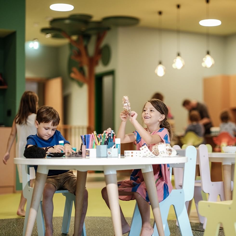 Bambini giocano e mangiano insieme a tavoli bassi in un asilo nido colorato e vivace.