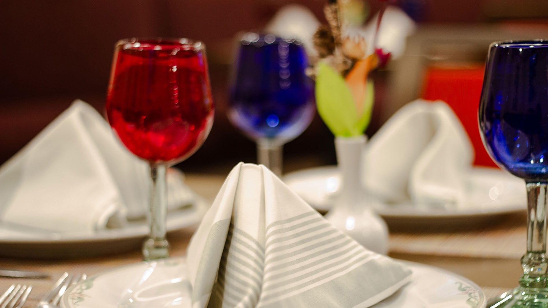 Close-up of a restaurant table setting with red and blue-tinted glassware at Camino Real Aeropuerto Mexico