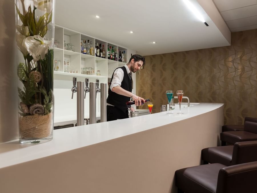 A bartender making drinks by the bar counter at Hotel Arianis