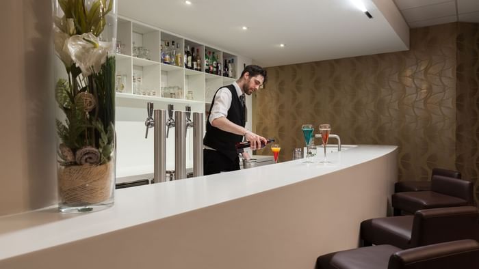 A bartender making drinks by the bar counter at Hotel Arianis