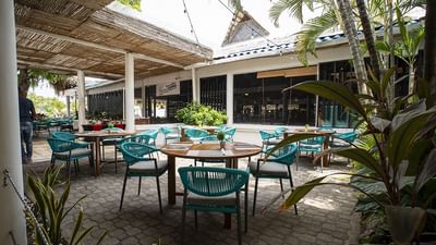 Outdoor dining patio with turquoise chairs and wooden tables surrounded by tropical plants at Playa Blanca Beach Resort