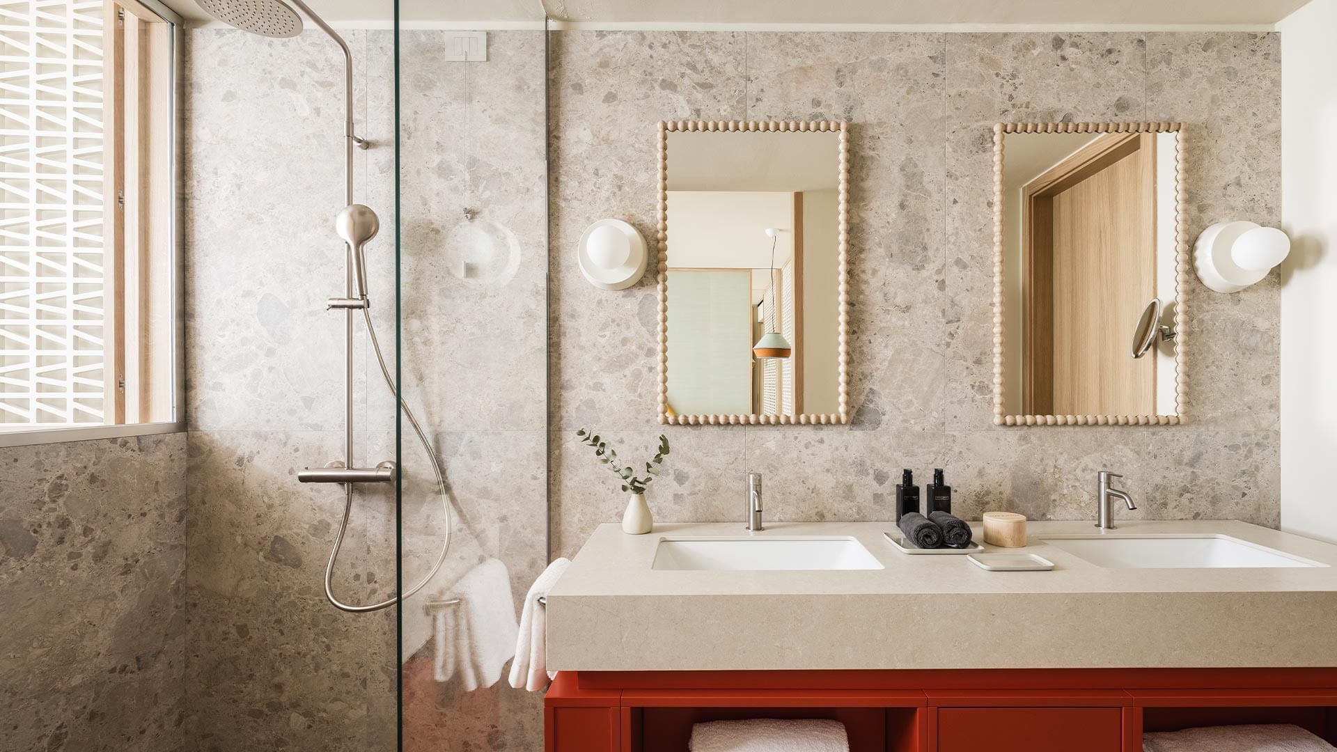 A modern bathroom with two sinks, mirrors, a showerhead, and a window with a view.