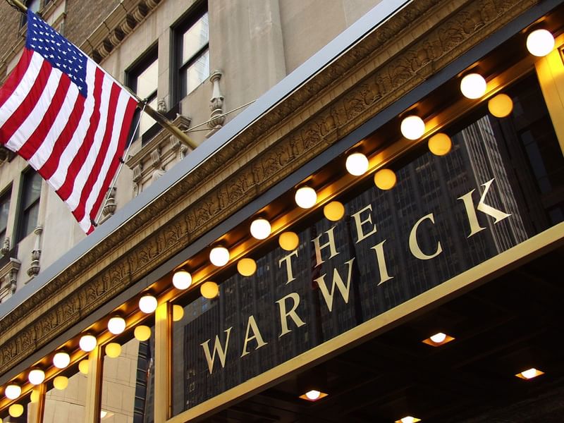 Facade of Warwick New York with an American flag and illuminated hotel sign board