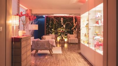 Interior of a cozy spa with wooden floors, cushioned chairs, a floral wall, and glass shelves.