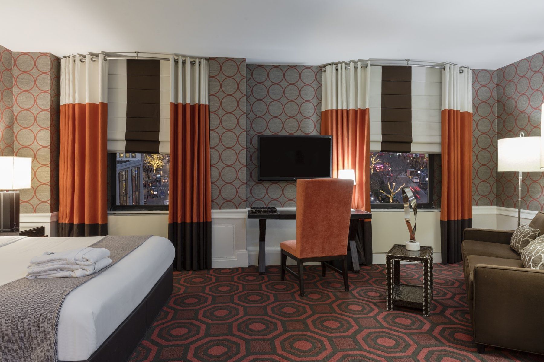A wide view of a hotel room with a bed, desk, chair, sofa, and TV.
