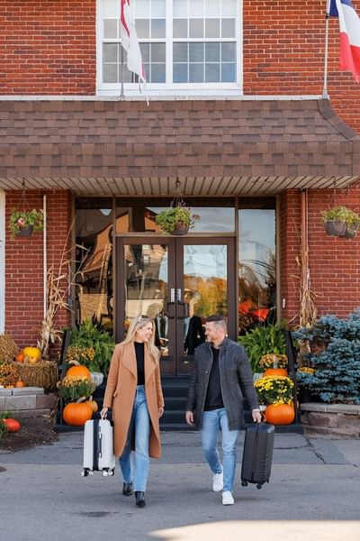 Smiling couple with luggage walking outside the red brick entrance with autumn pumpkin decorations at Rodd Royalty
