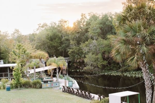 Wooden chairs overlooking a peaceful river surrounded by palm trees at sunset. Wekiva Island is a great spot for a romantic date in Orlando.