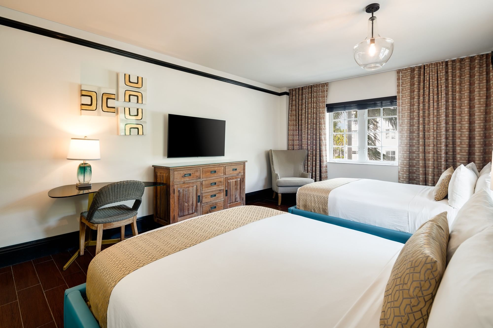 A hotel room with two beds, a TV, a desk, and a window.