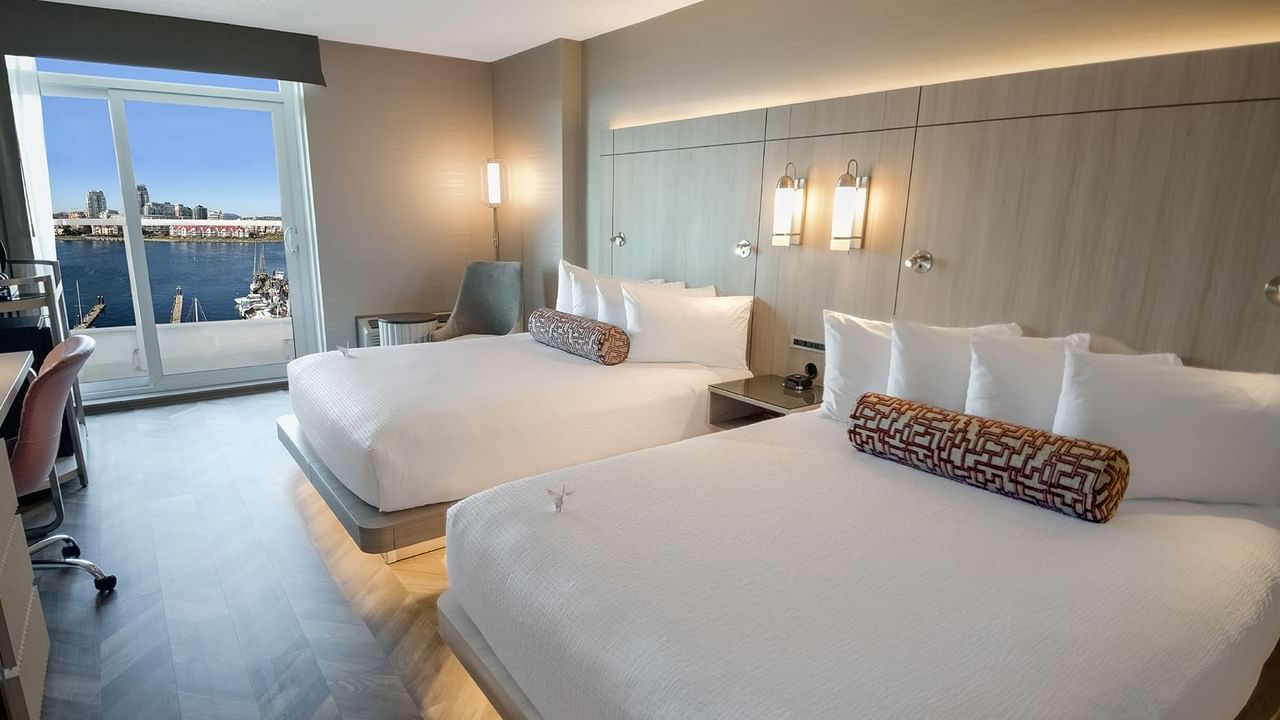 Hotel guestroom with two queen beds, work desk, chair, and an ocean view.