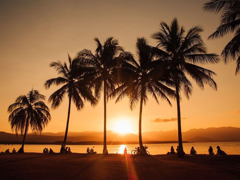 Distant evening view of Rex Smeal Park with people by sea near Pullman Port Douglas