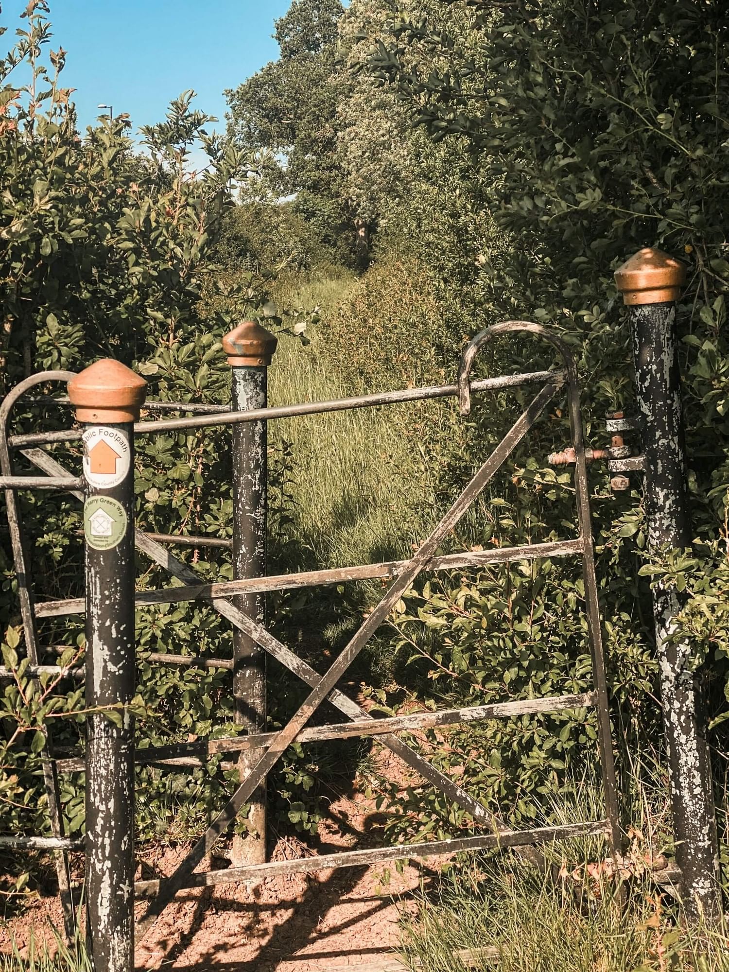 Rustic metal gate beside an overgrown green footpath leading to the lush nature trails around the Polo Club Hotel estate