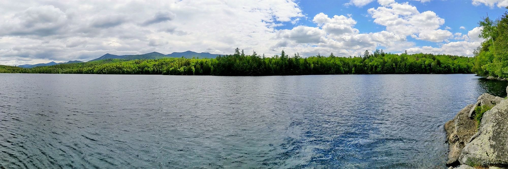 A wide-angle shoreline with calm waters and a mountain range in the distance.