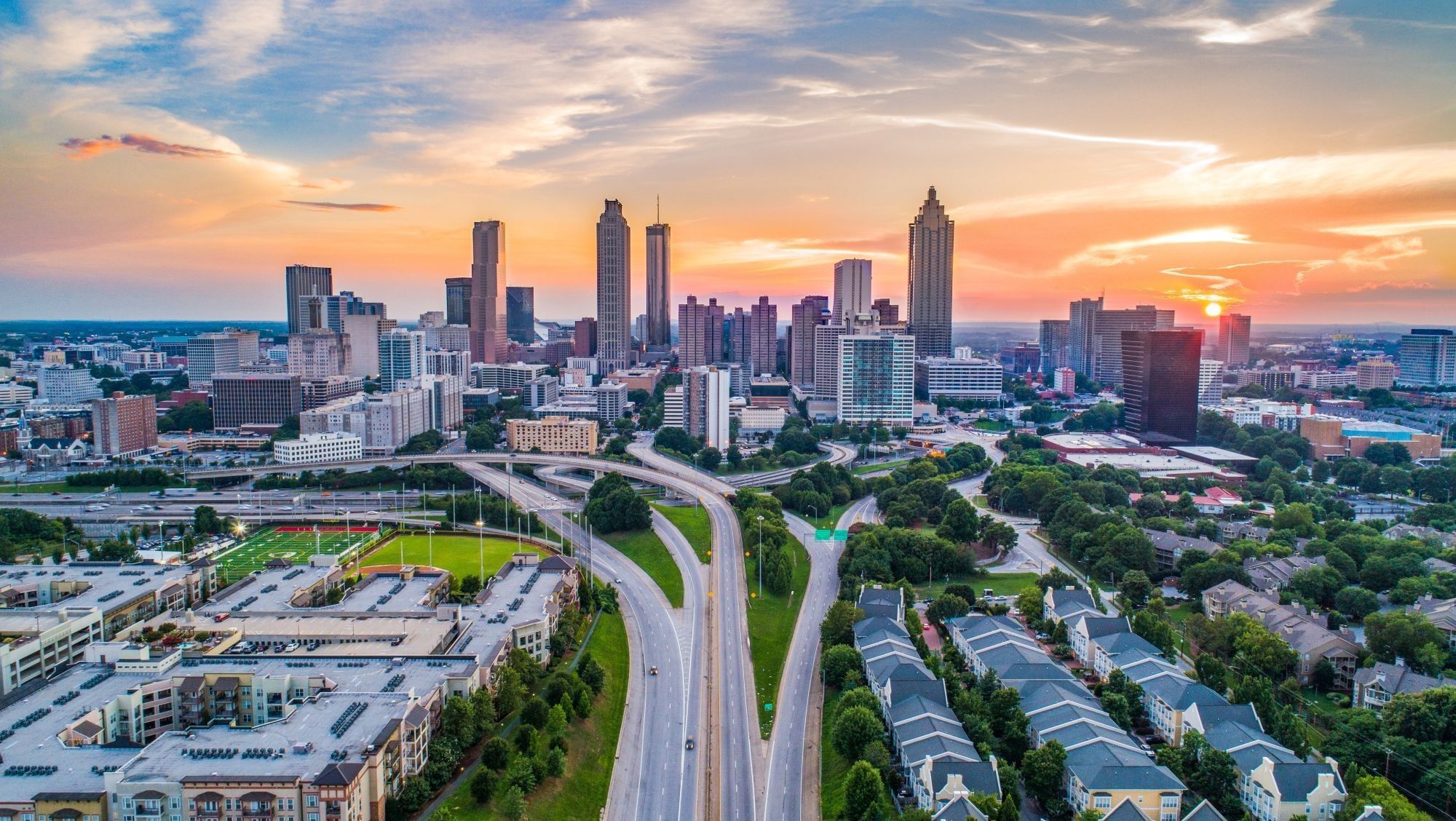 Aerial view of a city at sunset with a road and trees in the foreground.