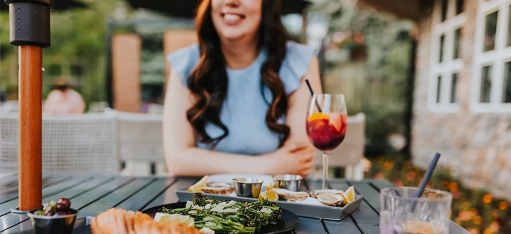 A person enjoys oysters and a cocktail on a patio in Canmore in May on a sunny day.
