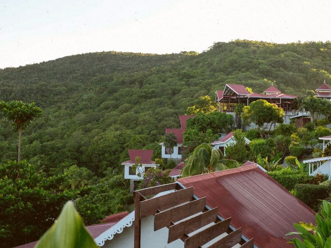Hillside resort villas with red roofs nestled among lush tropical vegetation and forested mountains under a soft sky.