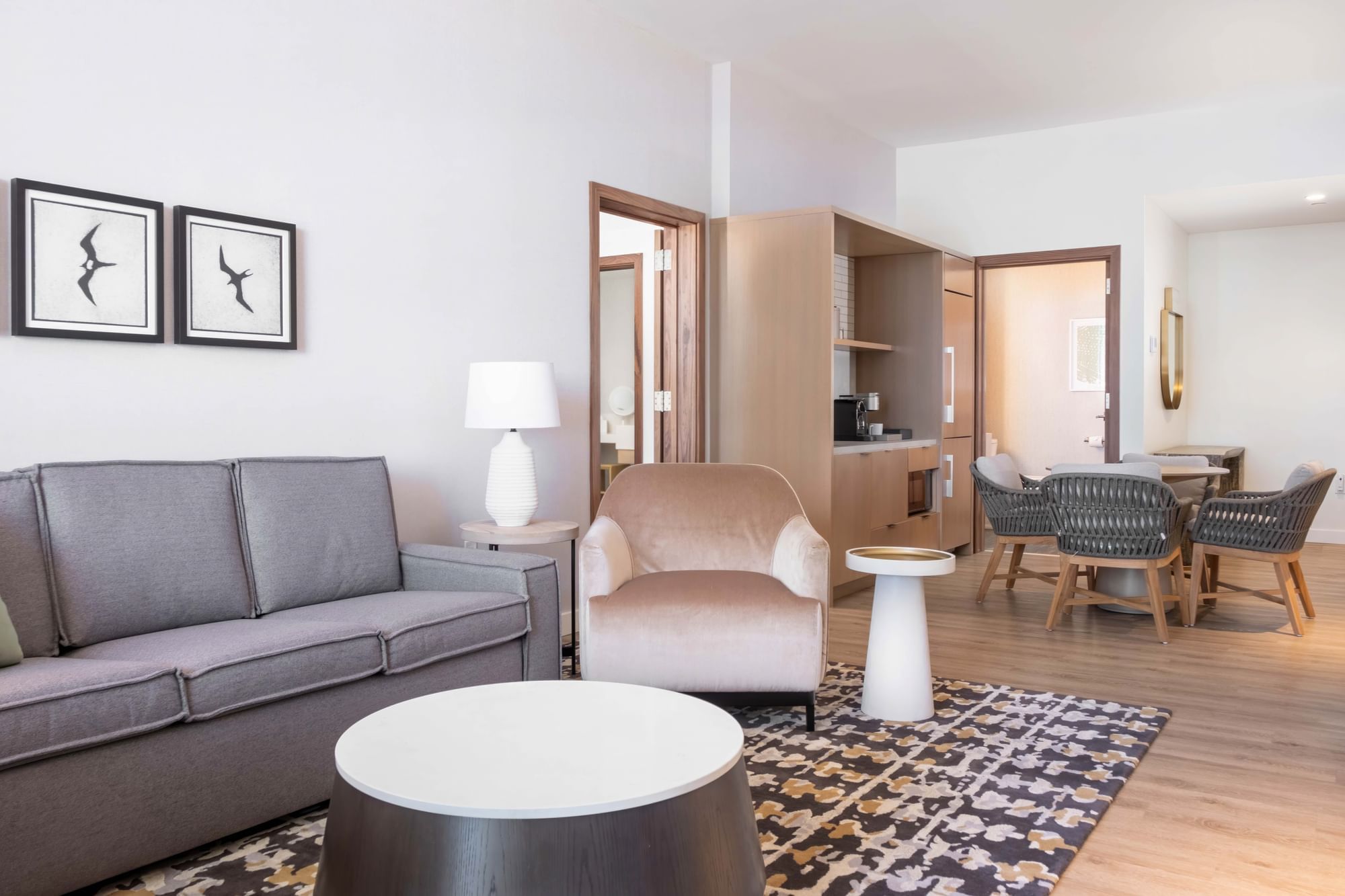 A wide view of a hotel suite's living area with a sofa, armchair, coffee table, and kitchenette.