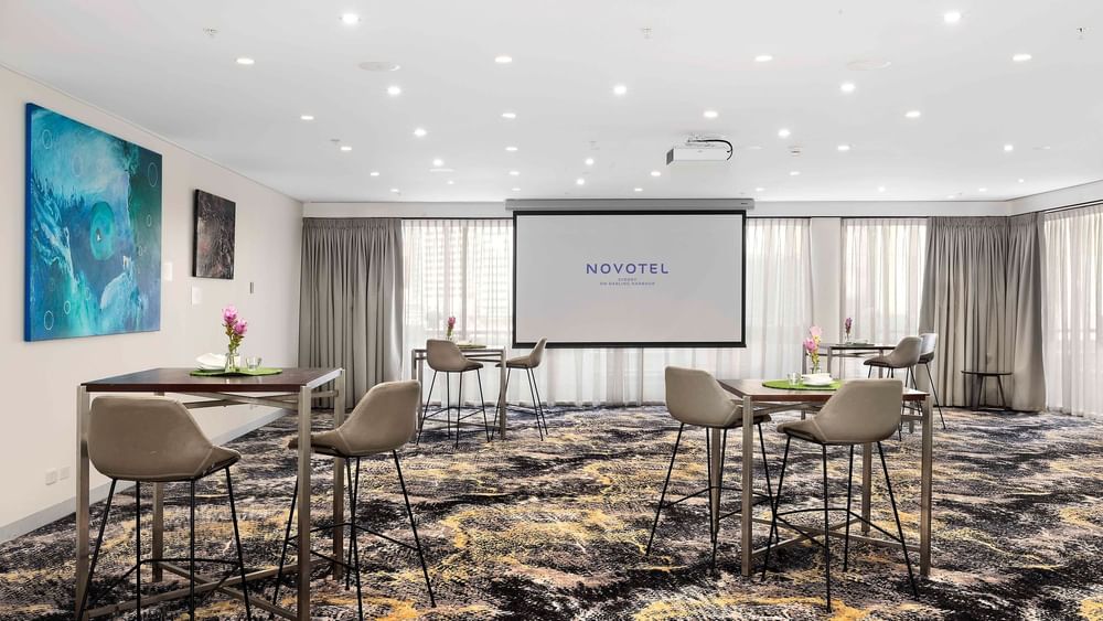 Table set-up with a projector screen and carpeted floors in The Barossa Room at Novotel Sydney on Darling Harbour