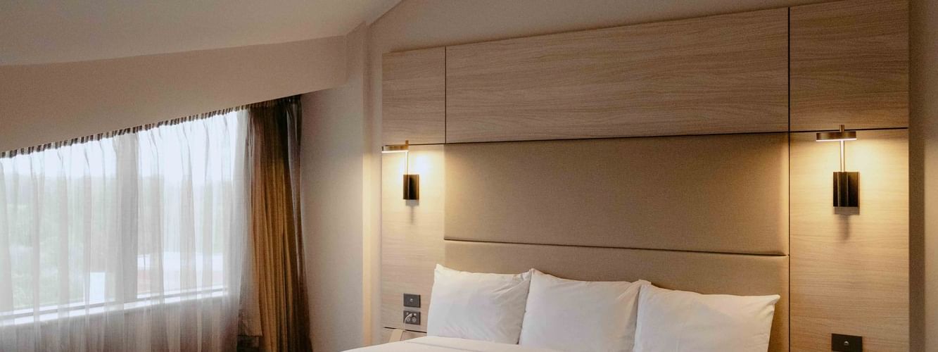 Plush bed by a window in the Executive King Suite at Novotel Sydney Parramatta, under warm light