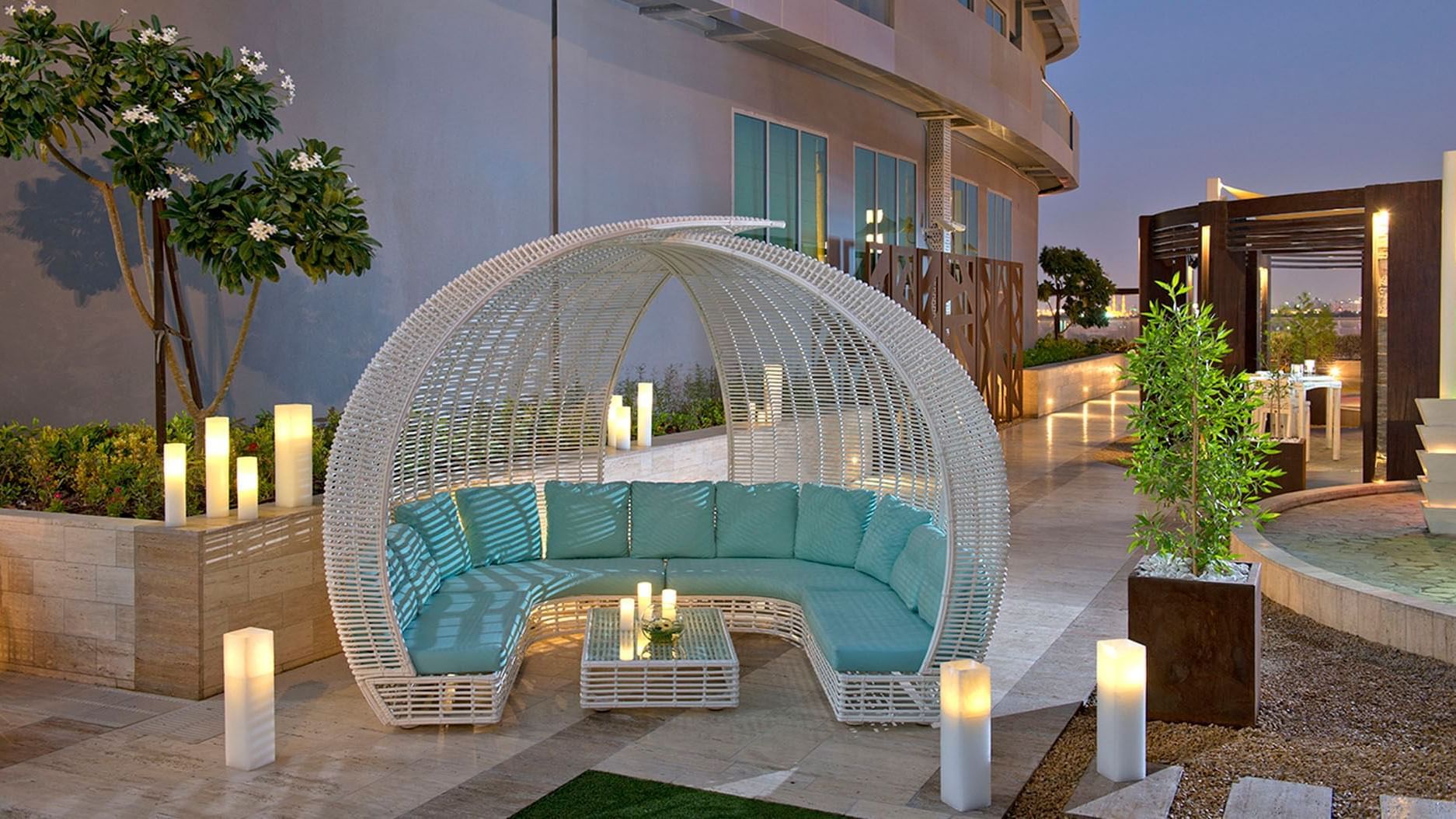 A patio with a white wicker couch and a blue cushion creates a cozy outdoor seating area at DAMAC Maison Dubai Mall Street