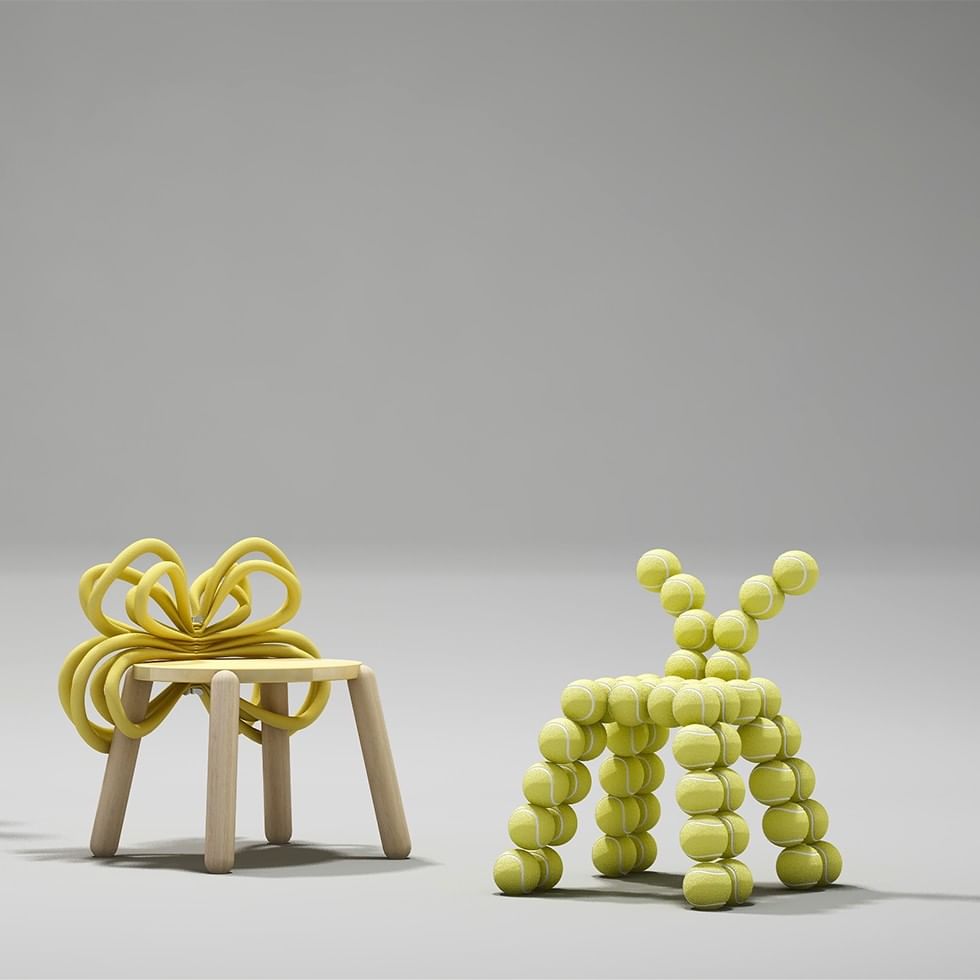 A chair and a dog-shaped sculpture, both made from yellow tennis balls, are placed on a gray surface.