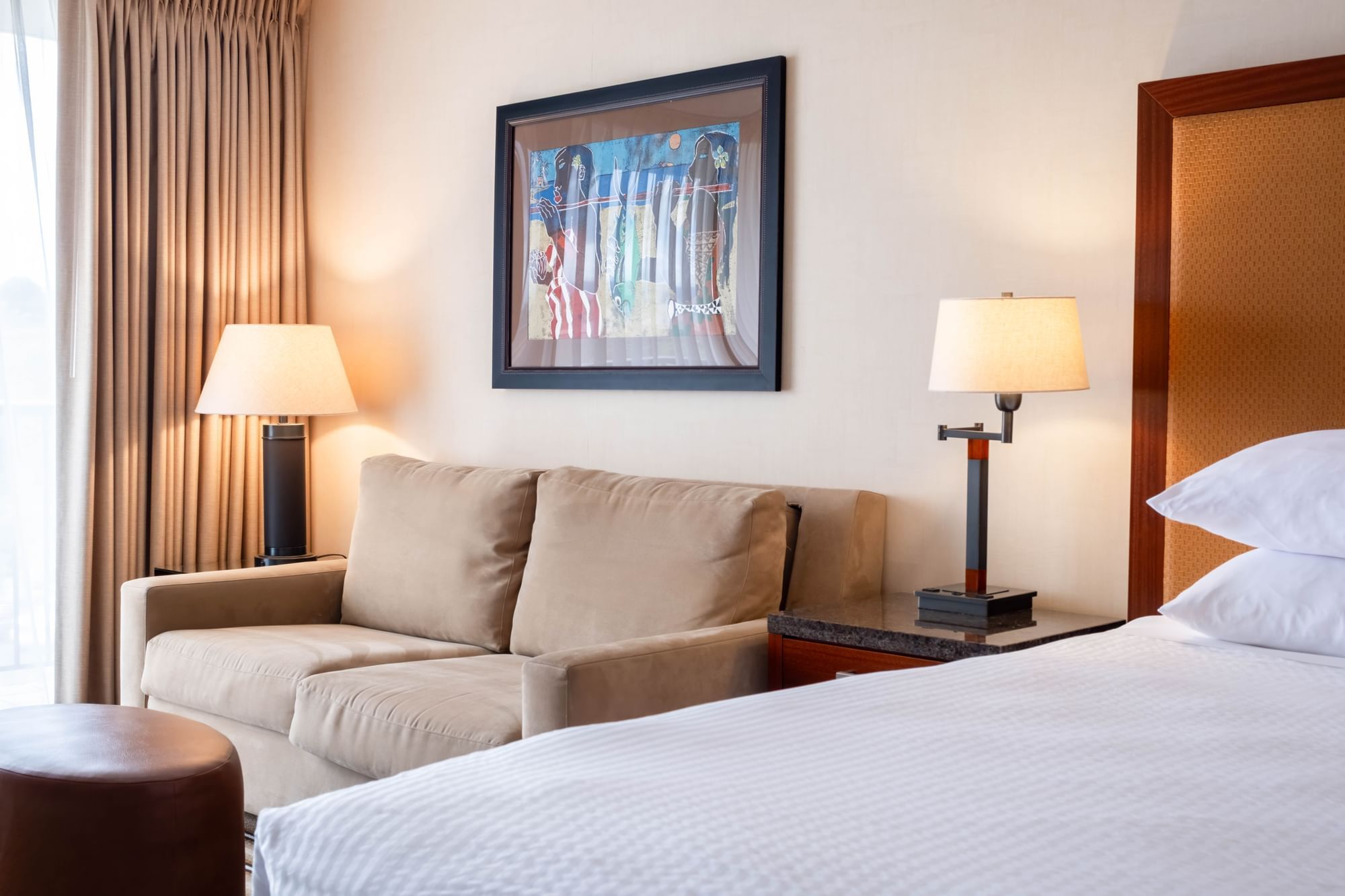 A hotel room with a bed, sofa, and artwork on the wall.