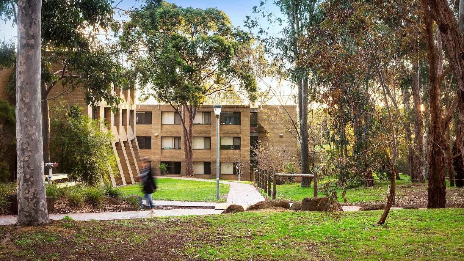 Student walking toward La Trobe University - Chisholm College building in a lush green park.