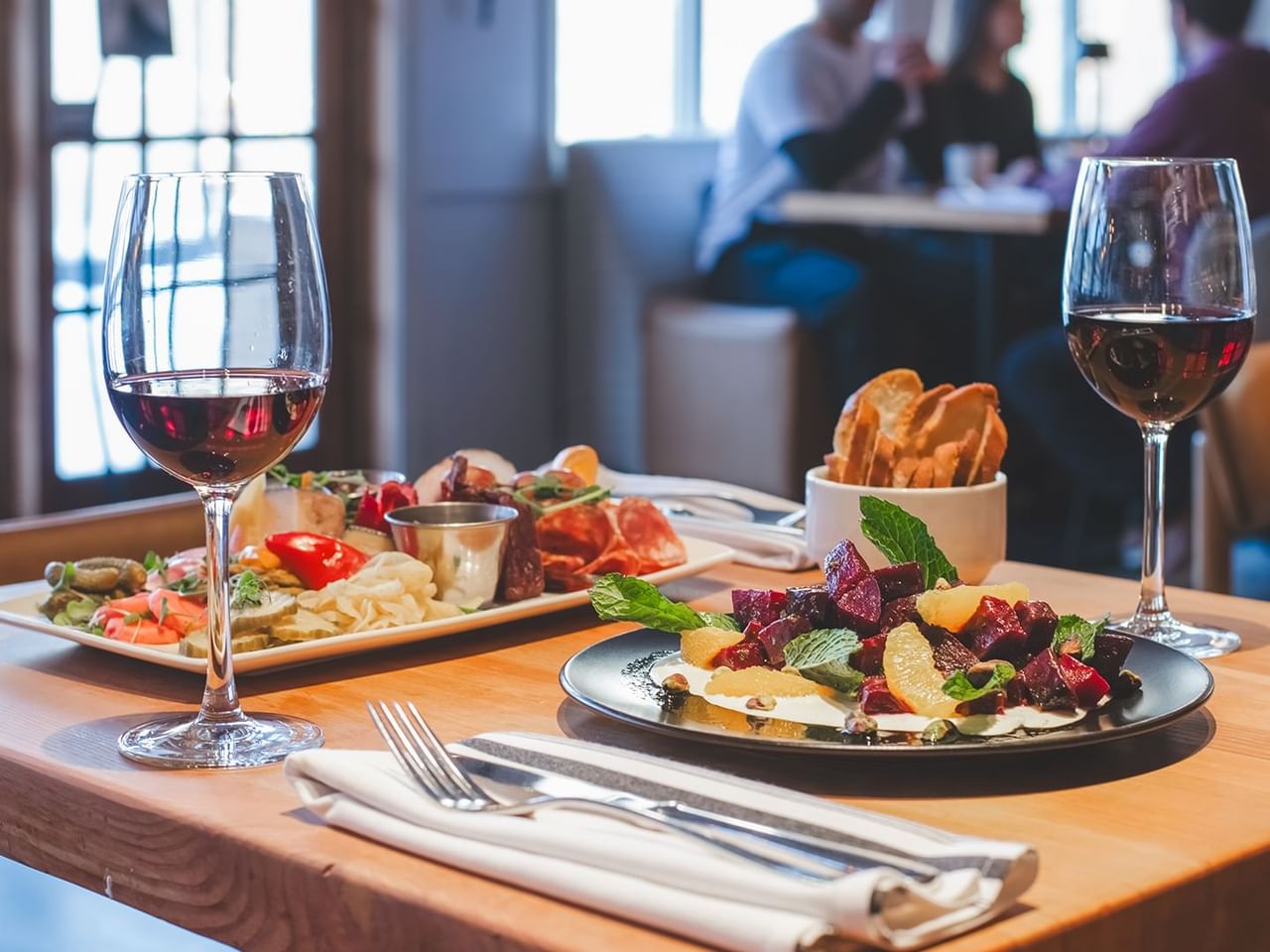 Two plates of food, two wine glasses, and cutlery on a wooden table.