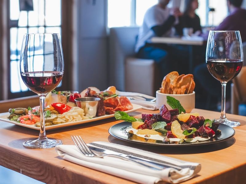 Two plates of food, two wine glasses, and cutlery on a wooden table.