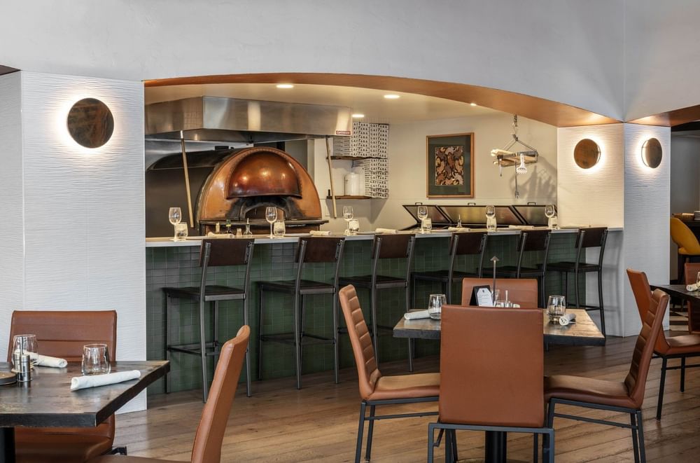 Chairs by a green tiled bar under an arched ceiling near a pizza oven in Gattara Restaurant & Patio at Warwick Denver