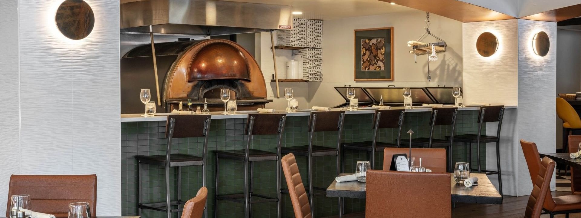 Chairs by a green tiled bar under an arched ceiling near a pizza oven in Gattara Restaurant & Patio at Warwick Denver