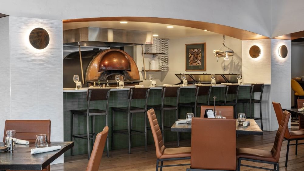 Chairs by a green tiled bar under an arched ceiling near a pizza oven in Gattara Restaurant & Patio at Warwick Denver